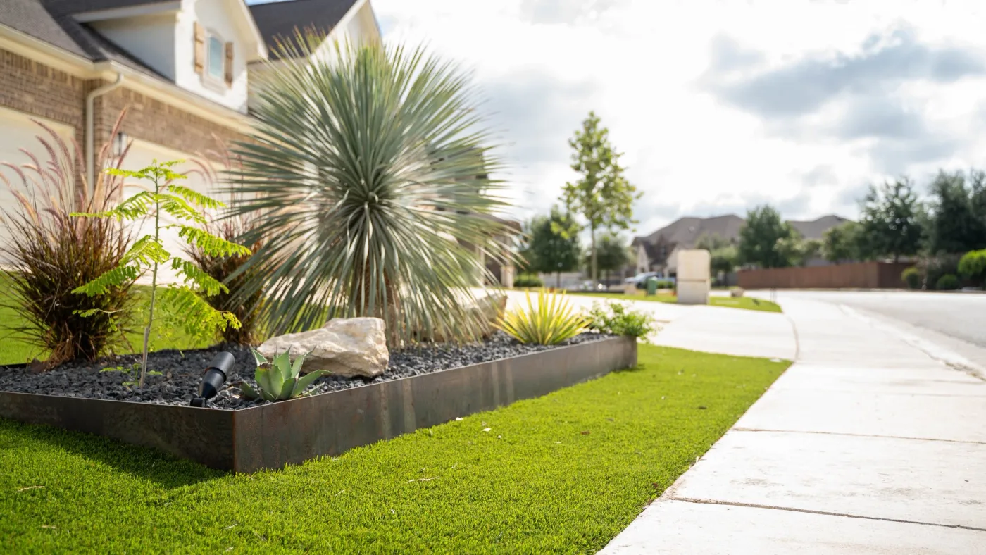 A steel-edged front bed planted with yucca, agave, and ornamental grasses over black gravel, beside a turf lawn