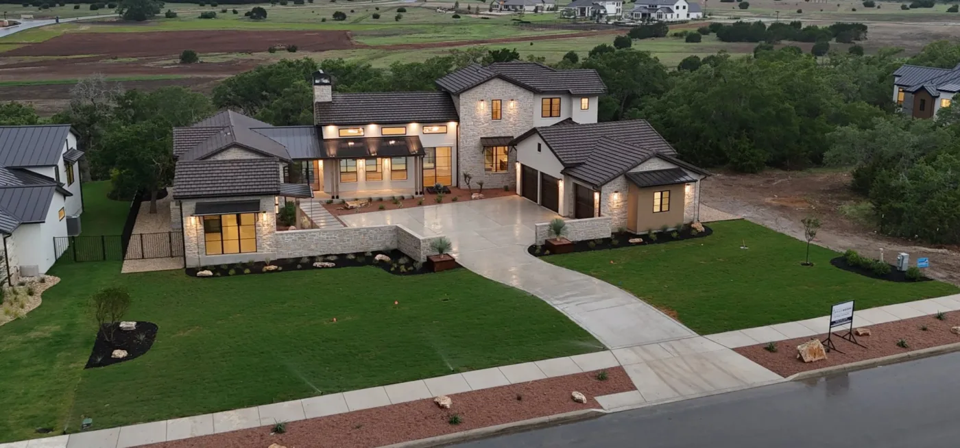 Aerial view of a large Hill Country home at dusk with a newly installed lawn, mulched beds, and sprinklers running