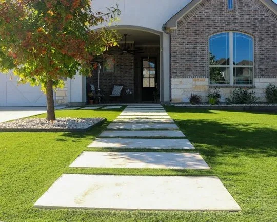 Large concrete pavers set into a healthy green lawn, leading to the front porch of a brick home