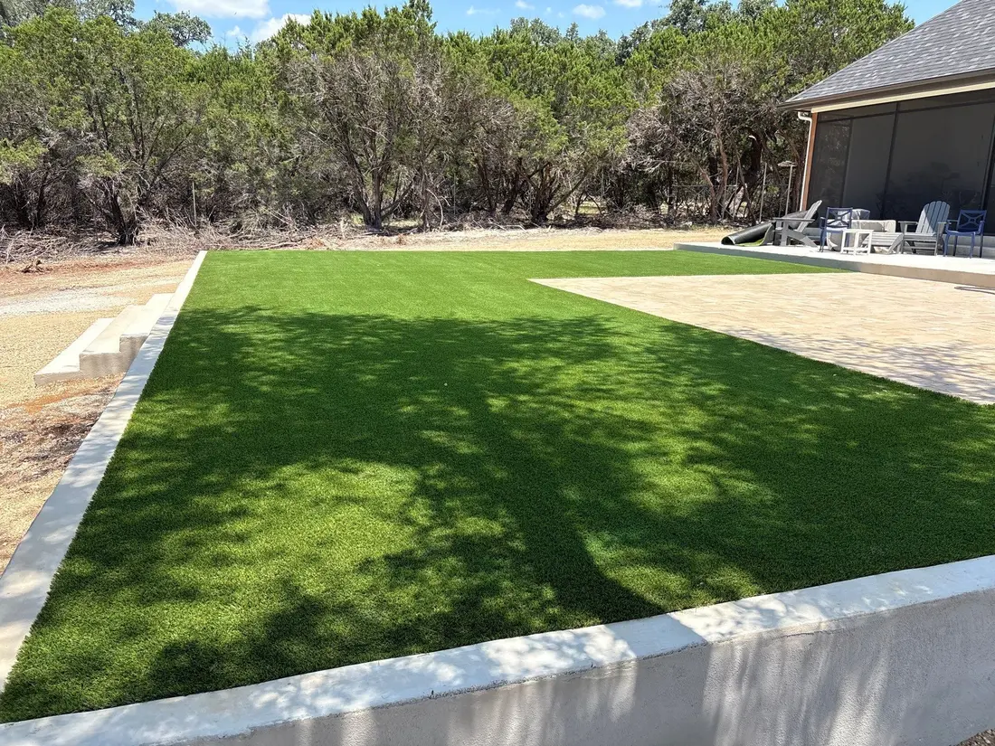 An artificial turf lawn edged with pavers and a limestone retaining wall on a Boerne property