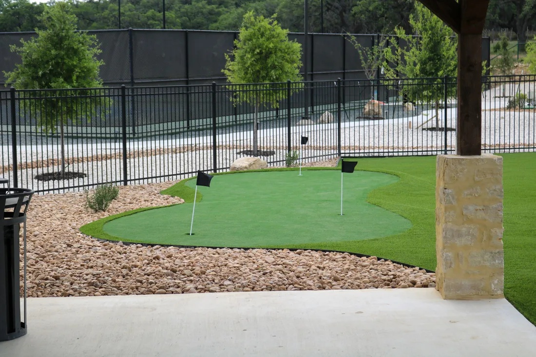 Artificial putting green with three cups, edged in dark mulch beds at Belle Oaks
