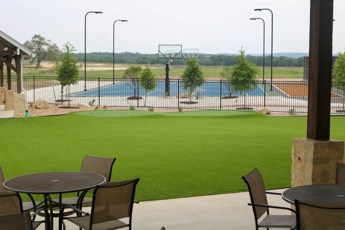 Open artificial turf lawn at Belle Oaks with basketball and tennis courts behind it