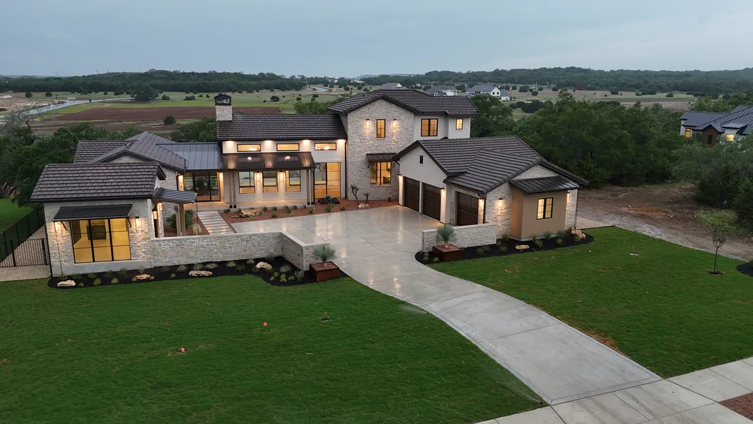 The finished Brad Moore custom home at dusk with lawn, planted beds, and lighting on