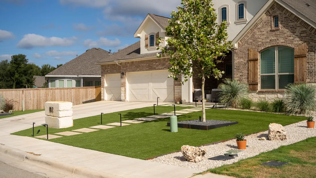 A finished front yard with a turf lawn, concrete steppers, and a young tree set in a gravel bed