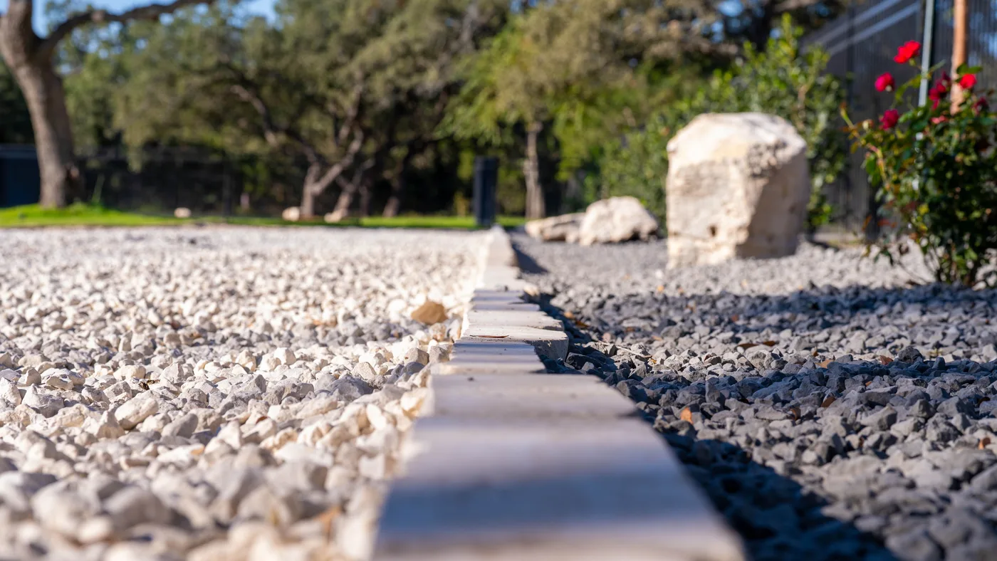 Steel edging separating white and black gravel beside a limestone boulder on a Spring Branch property