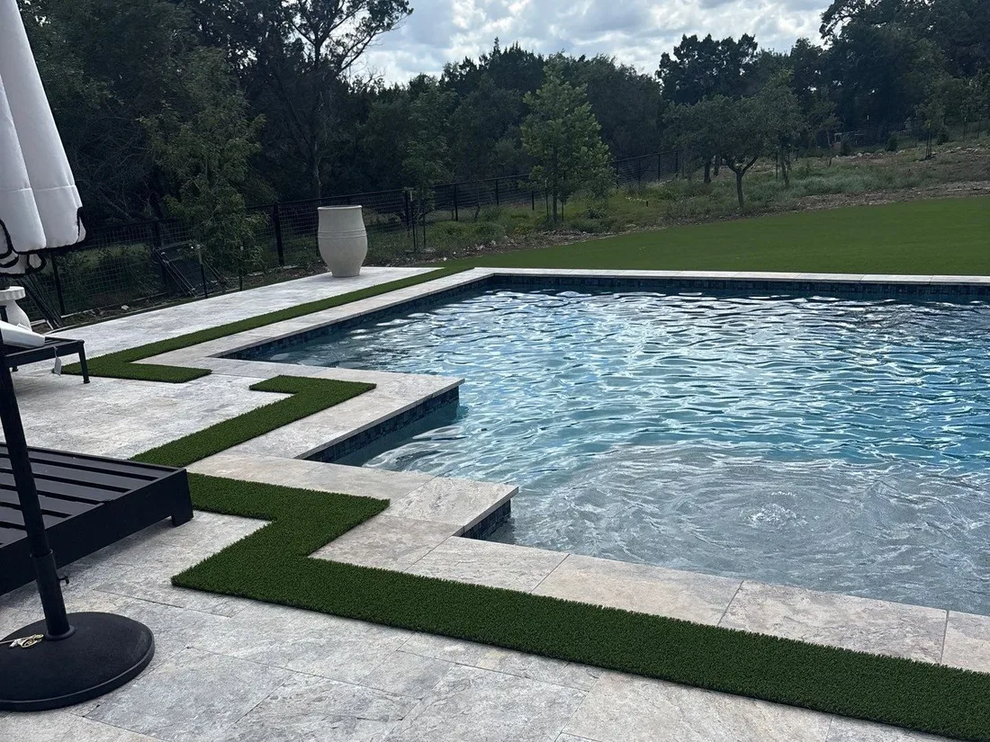 A pool edged in travertine with artificial turf set into the decking on a Spring Branch property