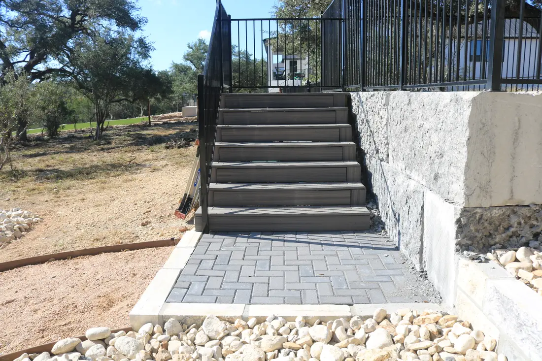 Paver steps with a black handrail, held by a cut limestone retaining wall