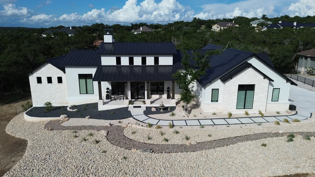 A modern Hill Country farmhouse with a xeriscaped front landscape design of gravel, agave, and a curved concrete walkway