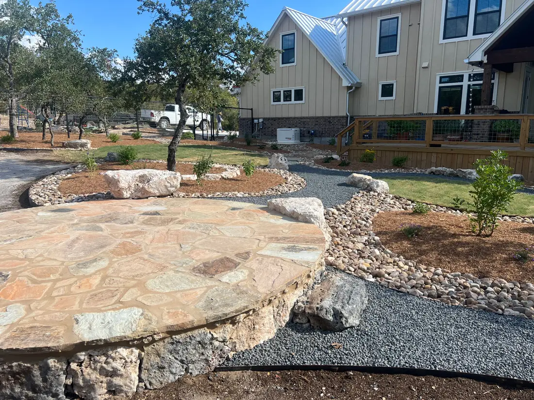 A circular flagstone patio raised on limestone, with gravel beds and a river rock swale running past new planting