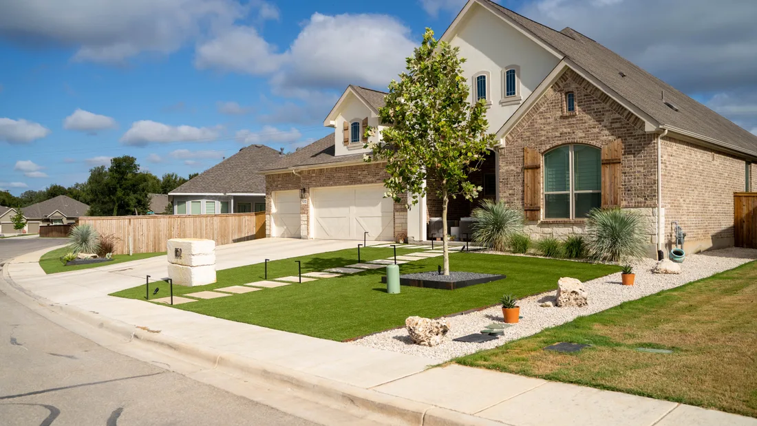A front lawn with concrete steppers and a young tree, edged clean against the drive