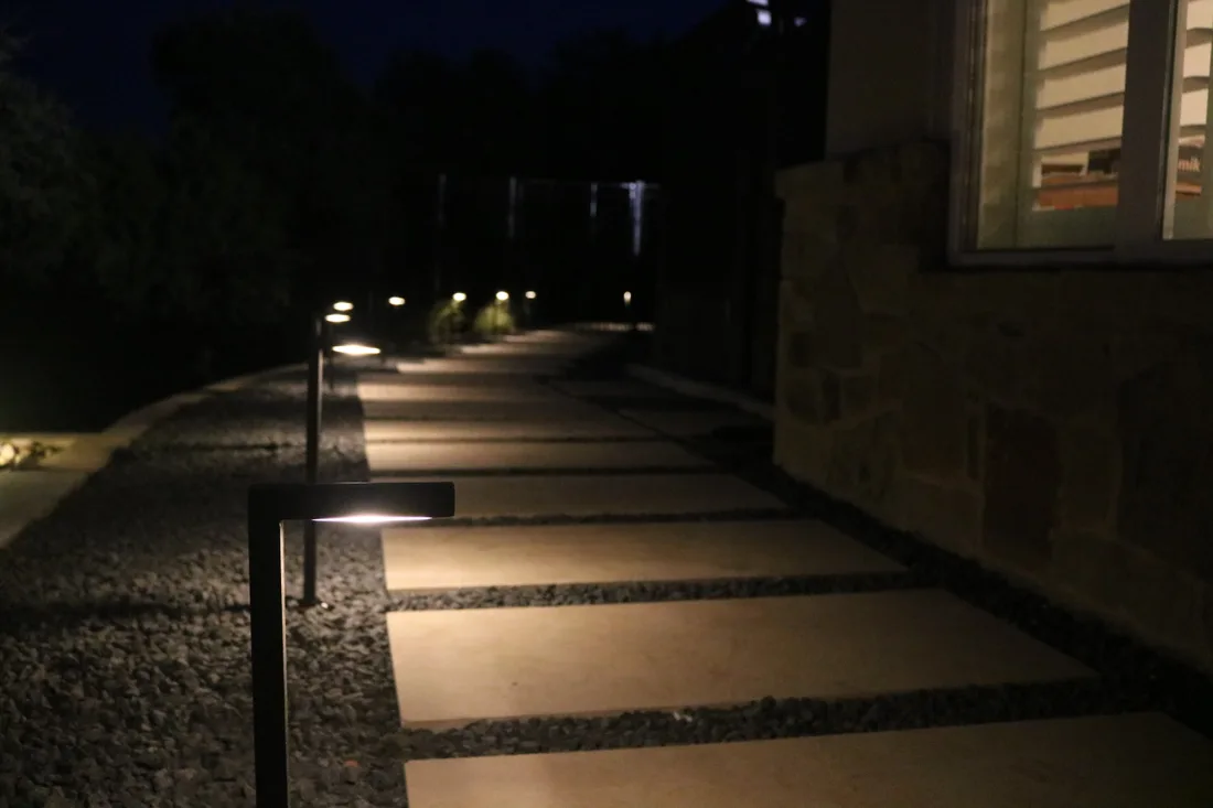 A path of concrete steppers lit at night by low path lights beside a limestone wall