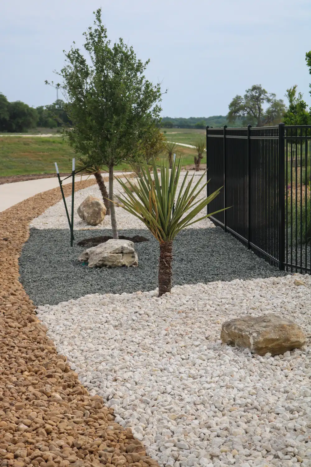 Yucca and limestone boulders set in white river rock along a black metal fence