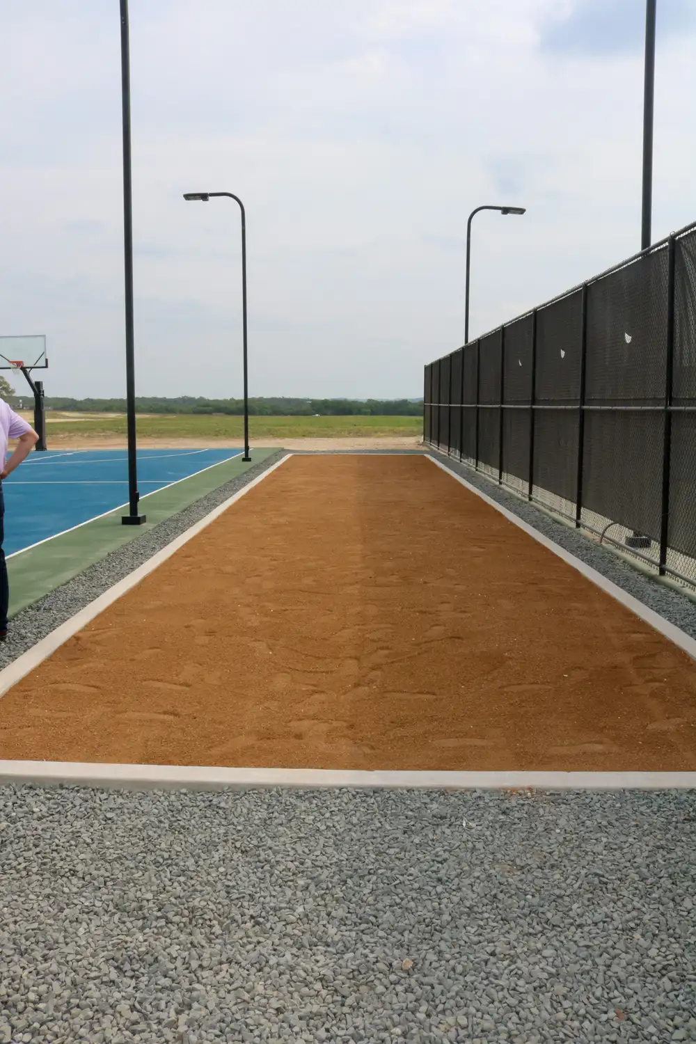 Decomposed granite sport court with a basketball hoop behind a windscreen fence
