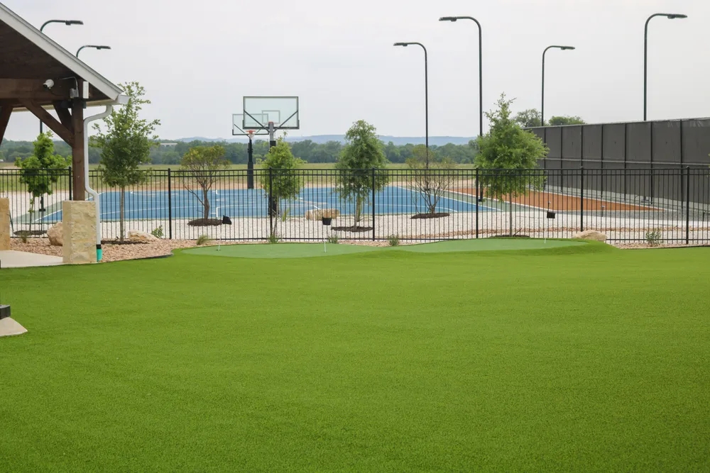 Open artificial turf lawn at Belle Oaks with a basketball court and the pool behind