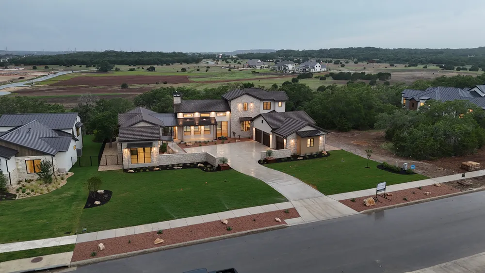 A finished Brad Moore custom home at dusk with new lawn, planted beds, and lighting on