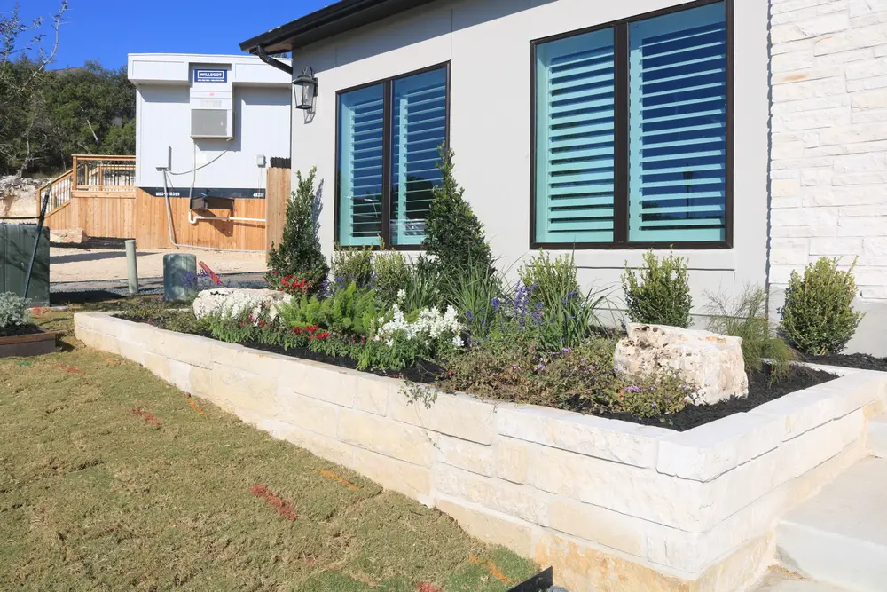 Cut limestone planter running along a house wall, planted with shrubs and perennials