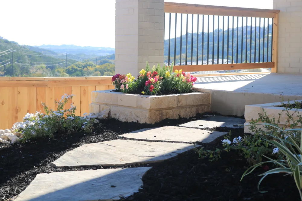 Flagstone path past a limestone planter of flowers, with the Hill Country beyond