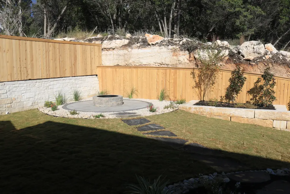 Terraced lawn held by a cut limestone wall against a cedar fence