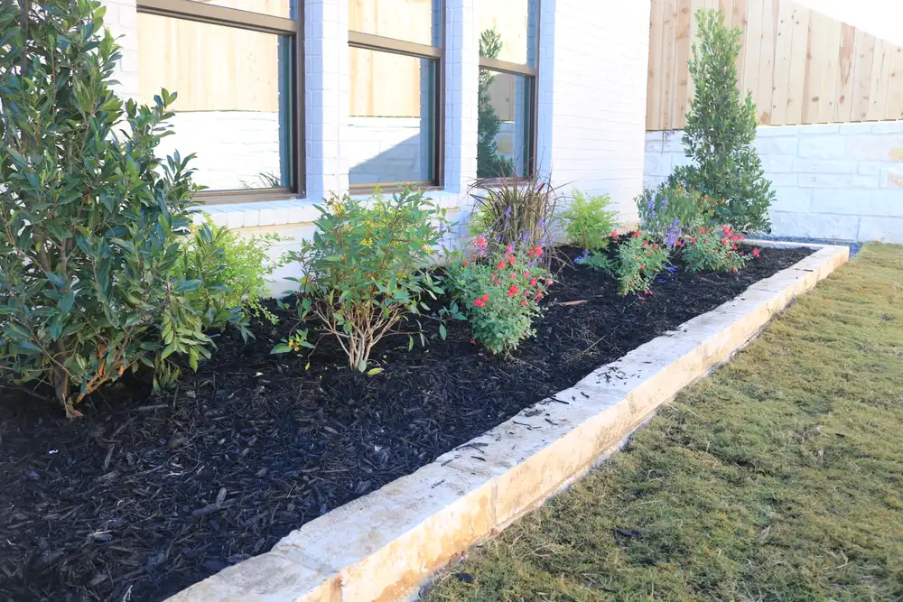 Foundation planting bed edged in cut limestone over dark mulch