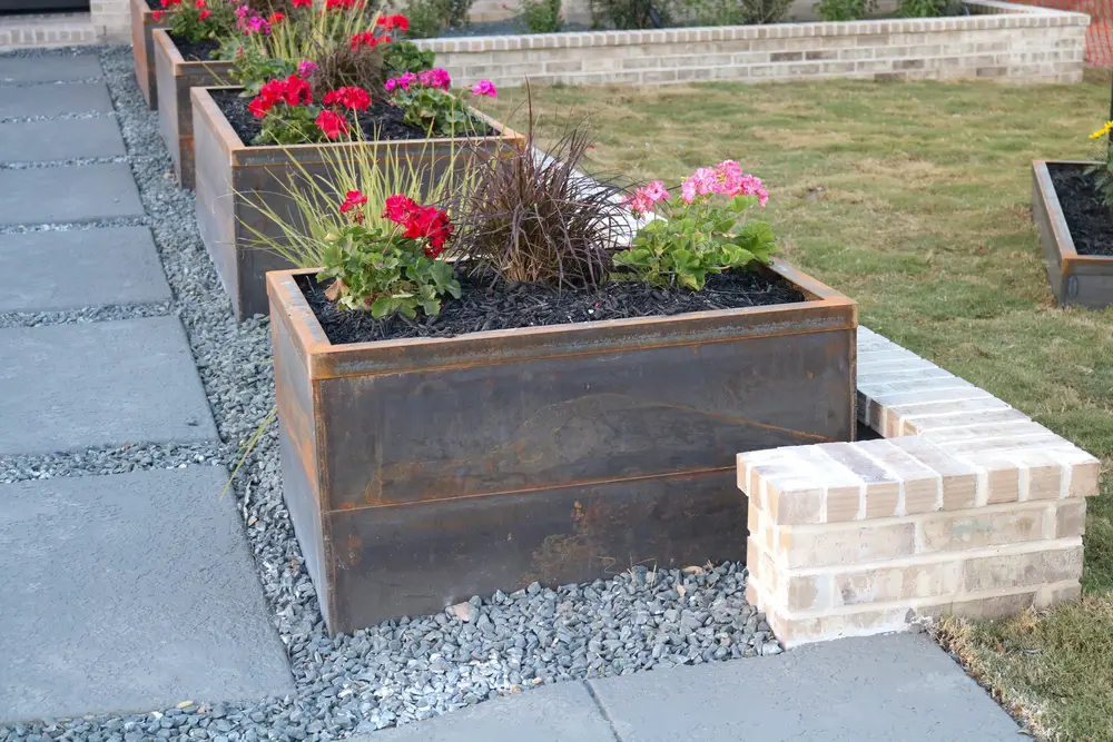 Corten steel planter against a brick column, planted with geraniums and grasses