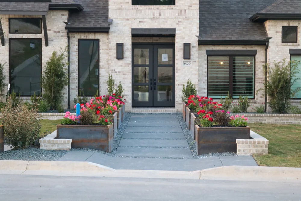 Model home entry doors flanked by corten steel planters in flower