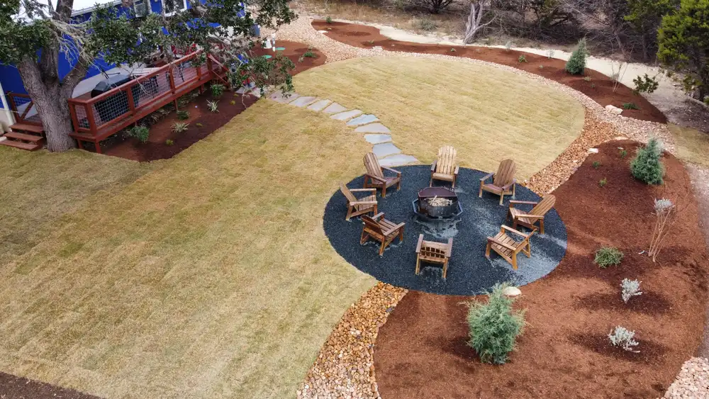 A fire pit ringed with Adirondack chairs on a flagstone circle, set in a new lawn