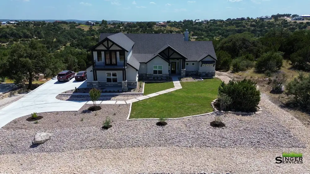 A custom Hill Country home with a new front lawn, gravel beds, and young shade trees