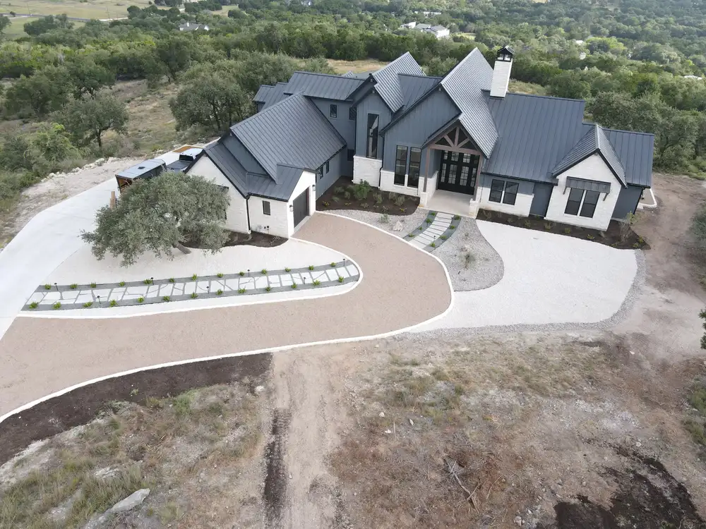 Aerial view of a large hilltop home with a curving drive and newly graded ground