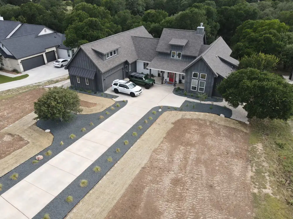 Aerial view of a home at the end of a long drive, with new beds along the approach
