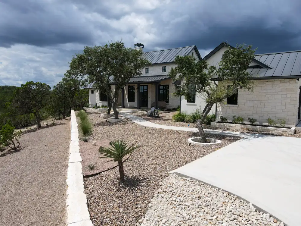 A young palm and limestone boulders set in gravel beds at the front of a Hill Country home