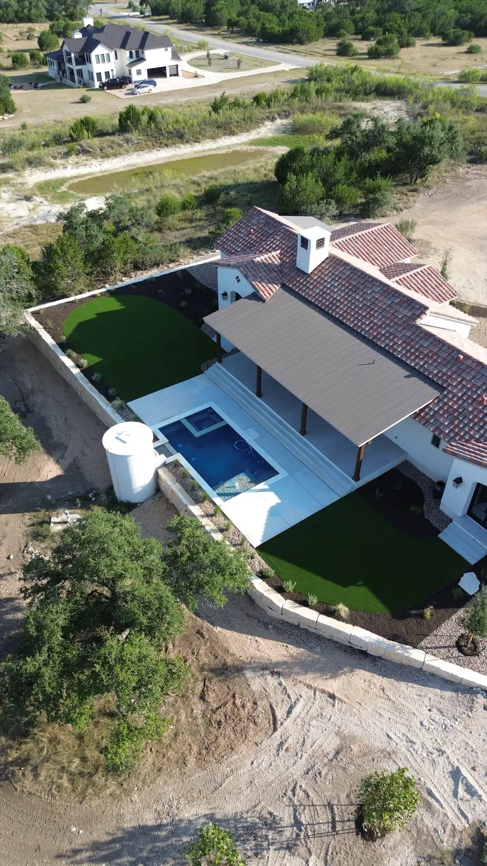 Aerial view of a backyard pool and turf lawn wrapped around a Hill Country home