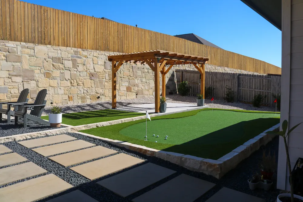 A backyard putting green beside a cedar pergola and a limestone wall