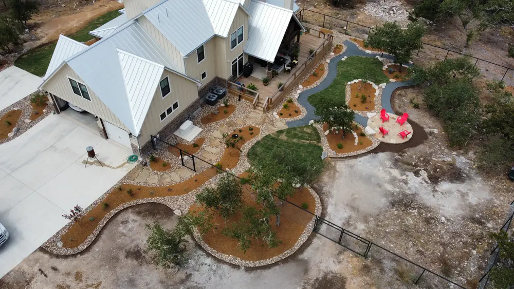Aerial view of curving stone edged beds and stepper paths wrapping a white metal roofed home