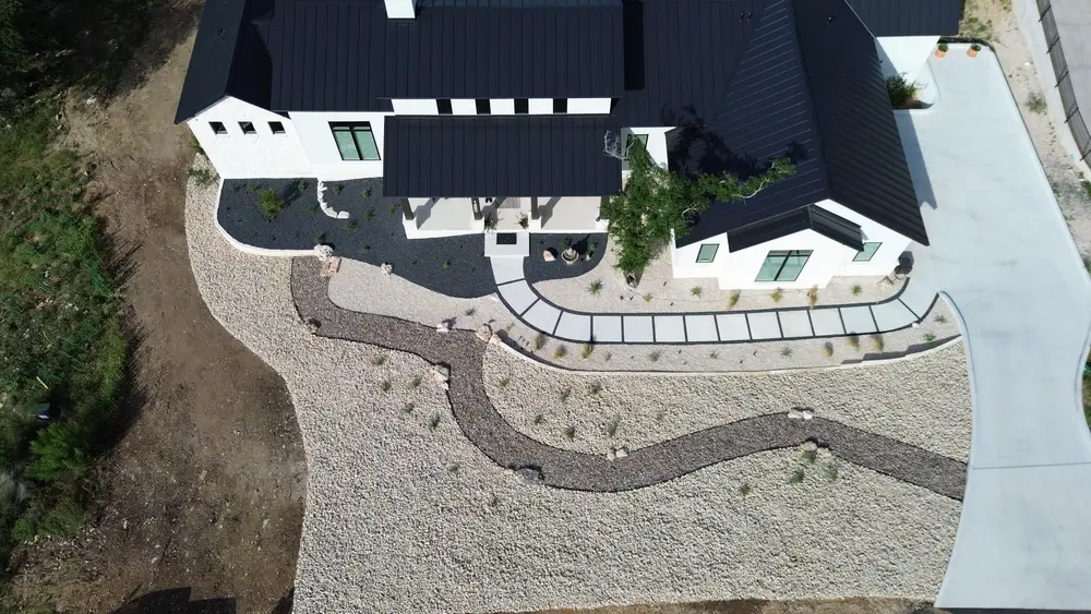 Aerial view of a curving stepper path set through pale gravel beside a modern Hill Country home