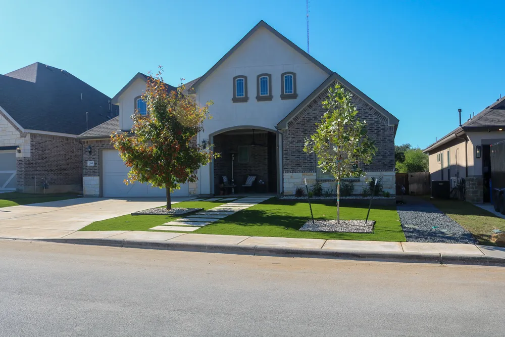 A two story home with a turf front lawn, a young shade tree, and a concrete entry walk