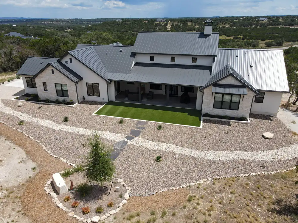 A modern farmhouse with a turf lawn set into a xeriscaped front of gravel and limestone boulders